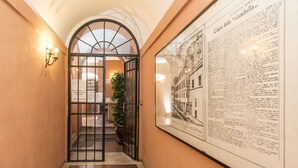 A hallway with a glass door leading to a room, a framed newspaper on the wall, and a potted plant. - Chiara in Pantheon apartment with terrace (Roma)