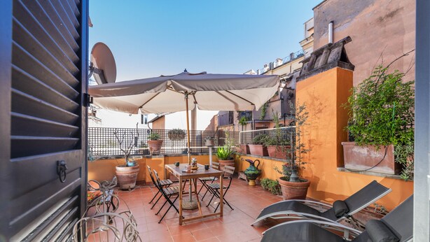 A rooftop terrace with a table, chairs, a large umbrella, and potted plants. - Chiara in Pantheon apartment with terrace (Roma)