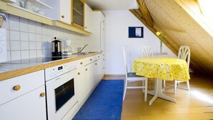 Une cuisine avec des meubles blancs, un plan de travail en bois et un coin repas avec une nappe jaune.