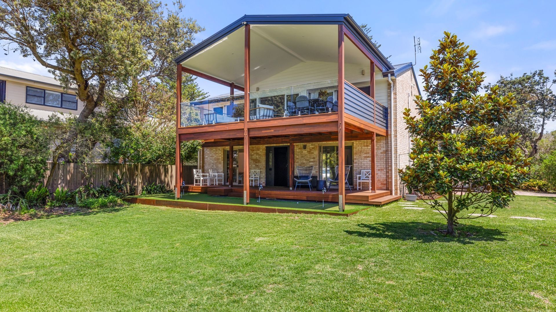 A two-story house with a balcony, a covered patio, and a well-maintained lawn.