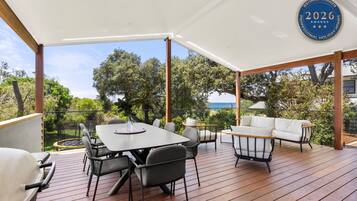 An outdoor deck with a table and chairs, a sofa, and a view of the sea.