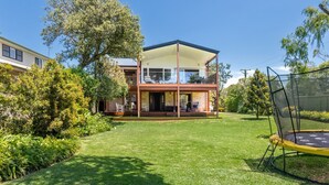 Una casa a due piani con un balcone, immersa nel verde di un prato curato e alberi.