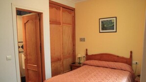 Un dormitorio con una cama de madera, una mesita de noche con lámpara, una puerta y un cuadro en la pared.