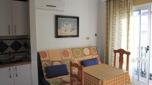 Una habitación con sofá, una mesa con mantel a cuadros, un cuadro en la pared y un balcón con cortinas estampadas.