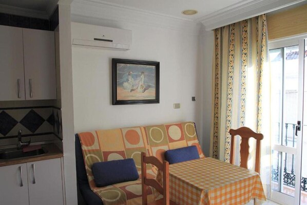 A room with a sofa, a table with a checkered tablecloth, a painting on the wall, and a balcony with patterned curtains. - Ana Hotel (Nerja)