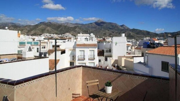 Una zona residencial con edificios blancos, tejados de tejas y una montaña al fondo.
