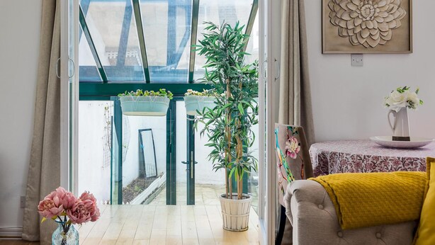 A room with a large window, a potted plant, a painting, and a table with a vase of flowers. - Duplex Apartment With Patio in Marylebone (London)