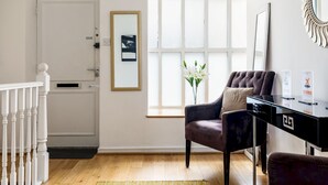 A modern living room with a dark brown leather sofa, a glass coffee table, and a white door with a small window. - Duplex Apartment With Patio in Marylebone (London)