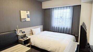 A hotel room with a bed, a desk, a chair, a TV, and a window with curtains.