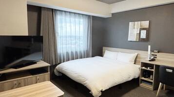 A hotel room with a bed, a desk, a TV, and a window with curtains.