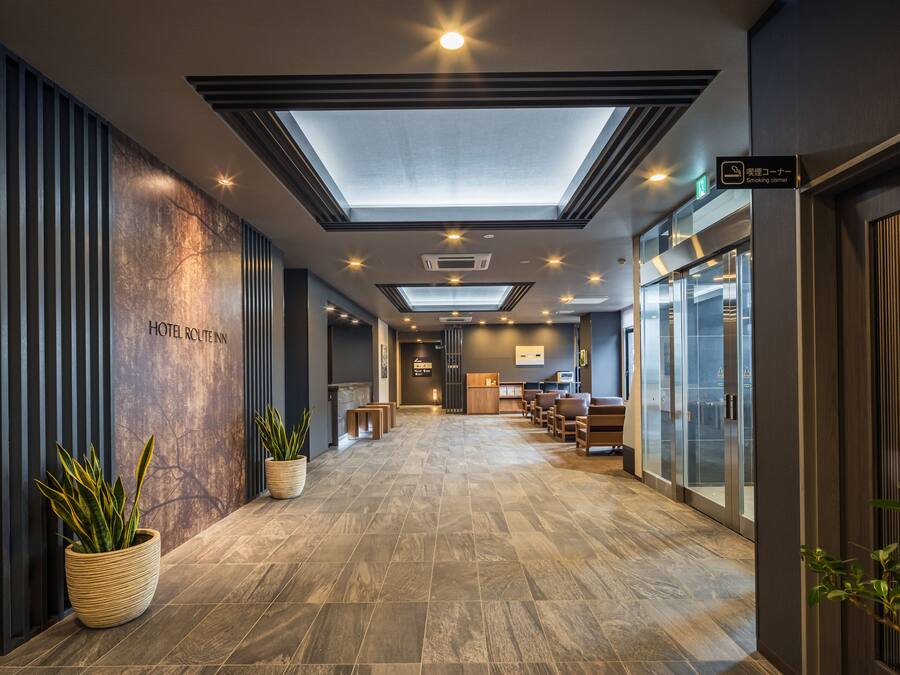 A modern hotel lobby with a skylight, potted plants, and a reception desk.