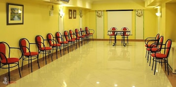 A conference room with rows of chairs and a table, yellow walls, and a projector screen.