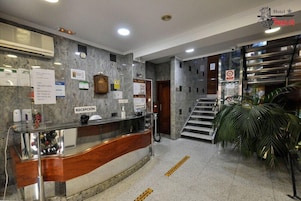 A hotel reception area with a marble wall, a reception desk, a staircase, and a sign indicating a no-smoking policy.
