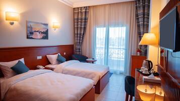 A hotel room with two beds, a TV, a desk with a lamp, and a painting on the wall.