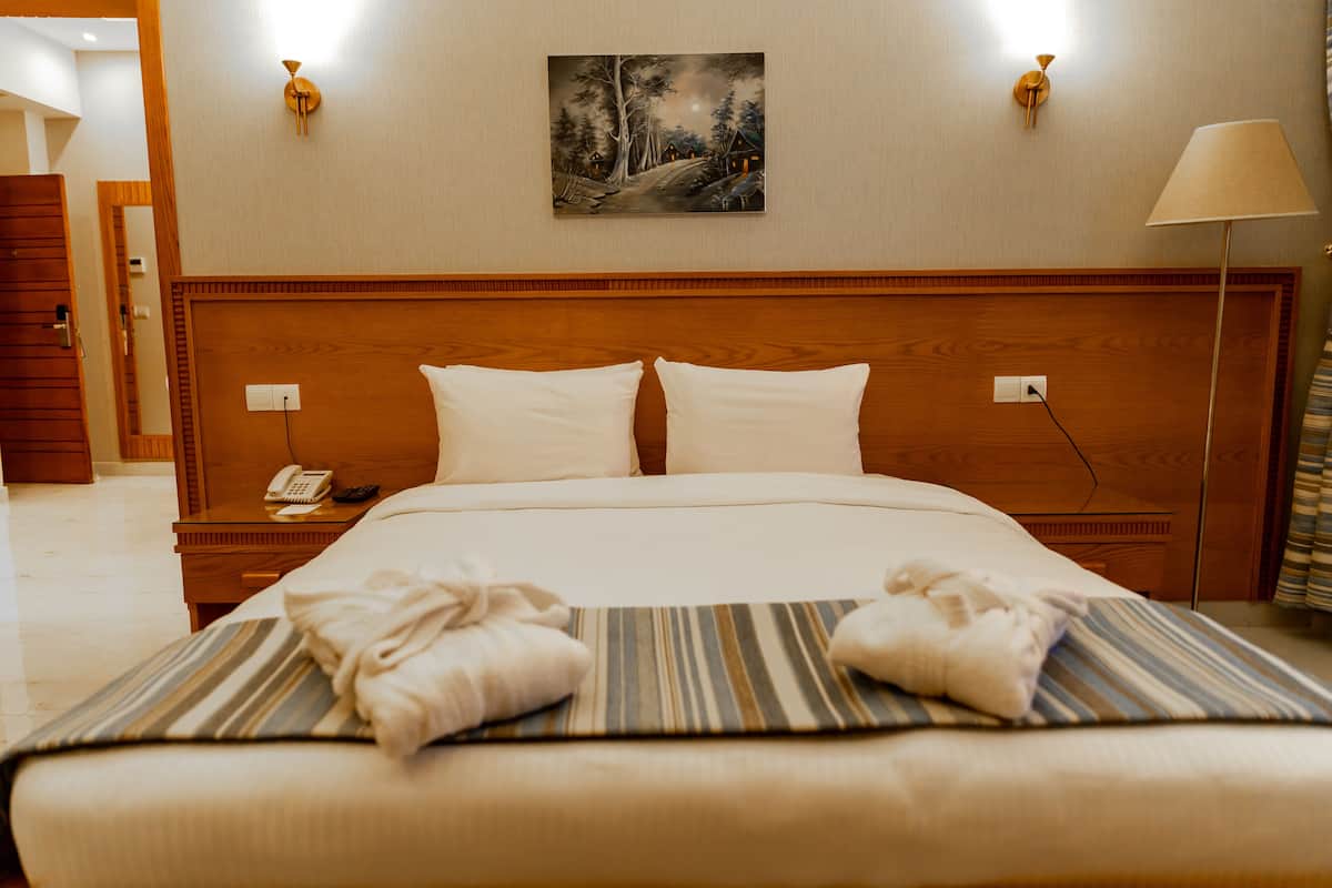Una cama bien hecha con sábanas blancas, un edredón a rayas y dos toallas dobladas sobre la cama.