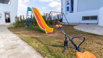 A playground with a yellow and red slide, swings, and a seesaw.