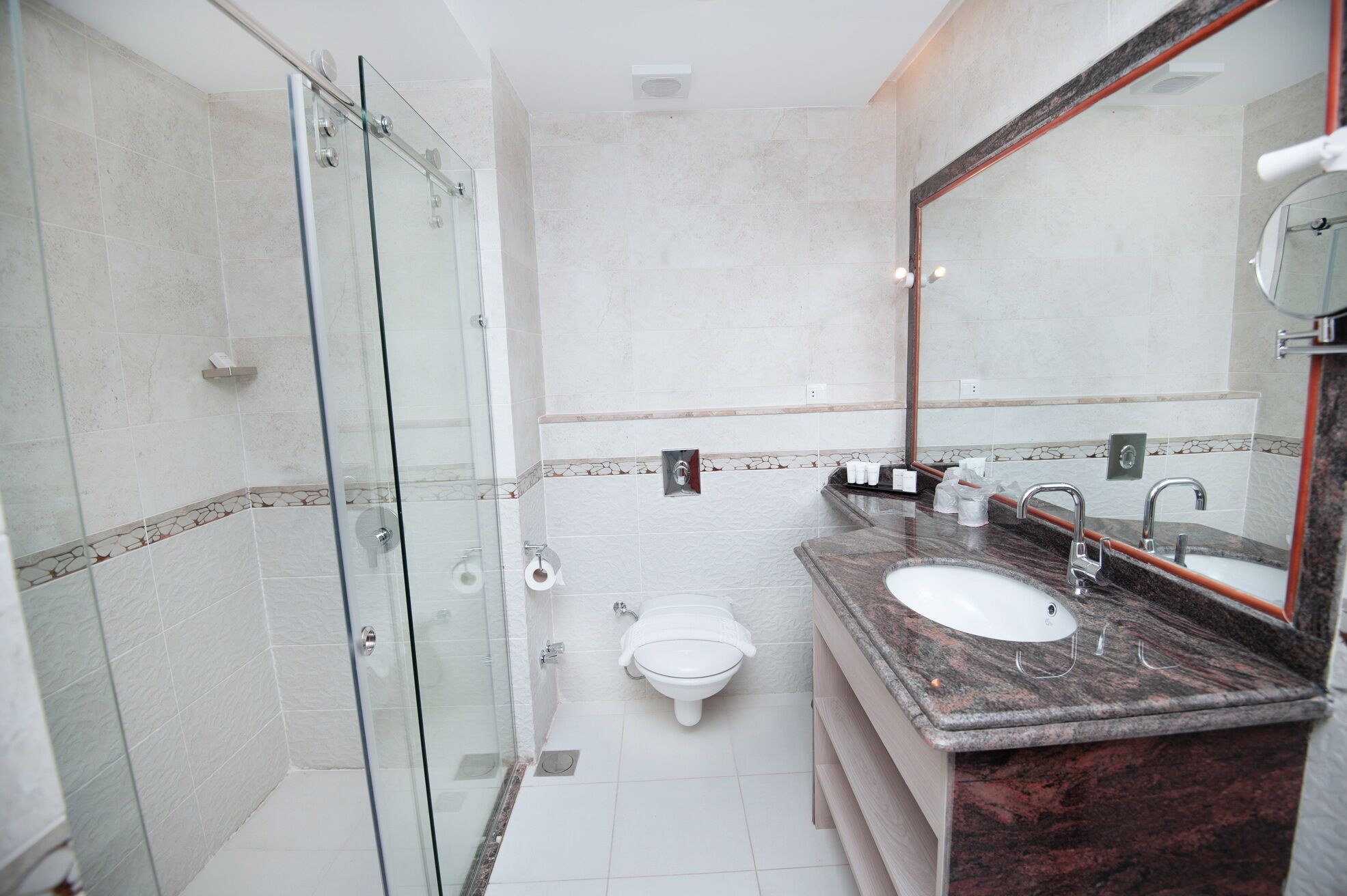 Un baño moderno con ducha envuelta en cristal, inodoro blanco y lavamanos de mármol con un espejo grande.