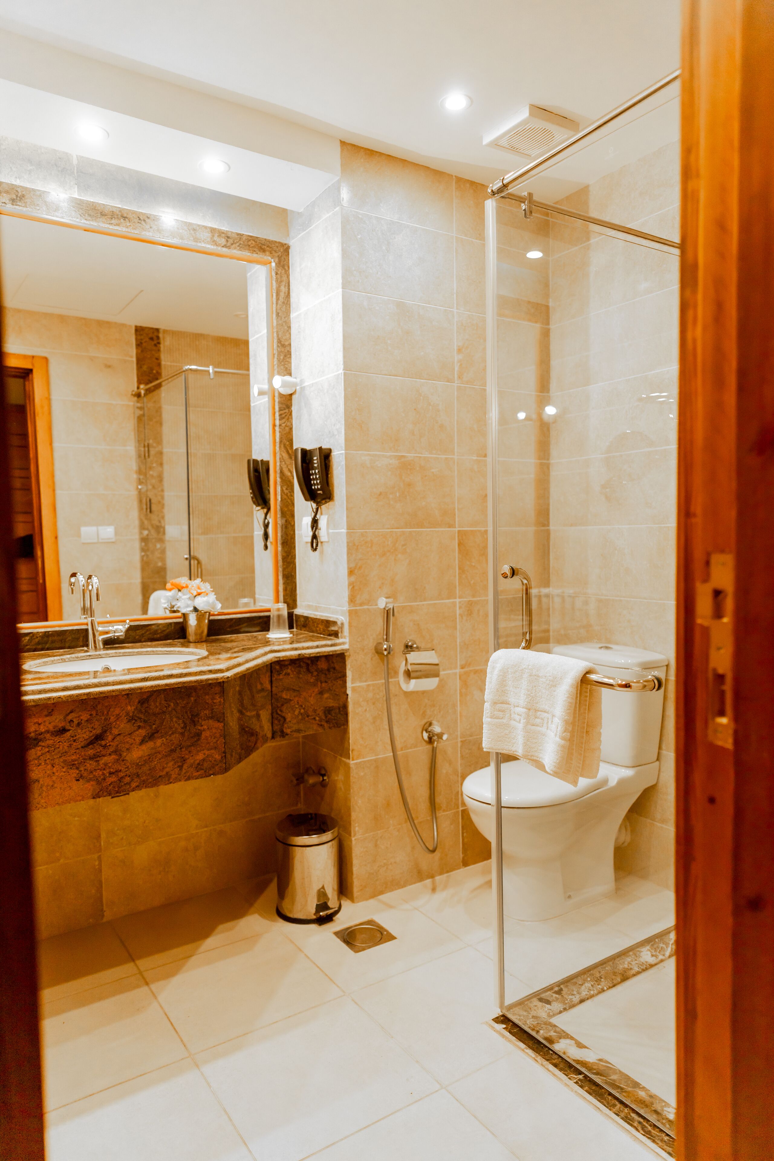 Un baño moderno con ducha envuelta en vidrio, lavabo de mármol y un inodoro con una toalla sobre el asiento.