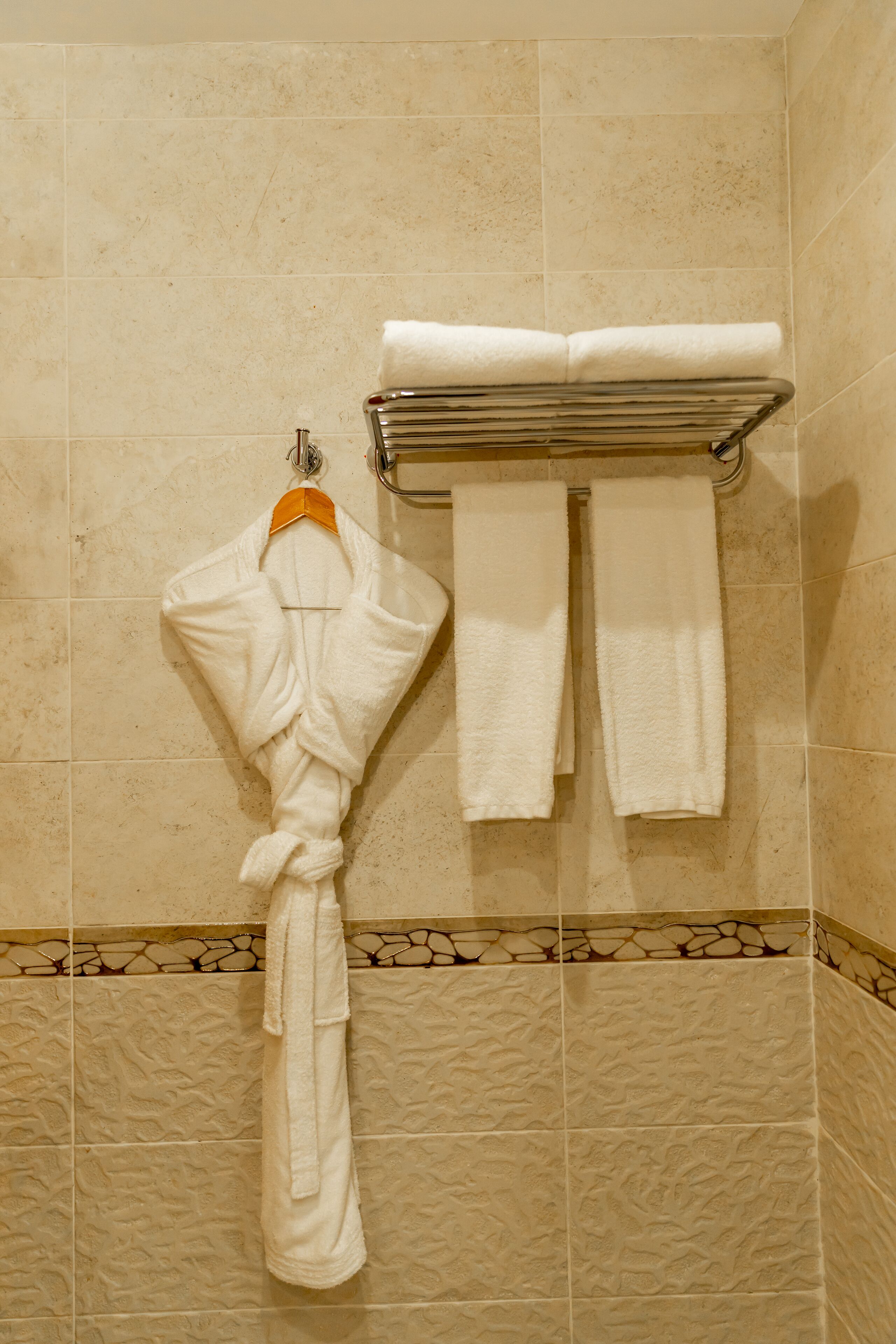 Casa de banho com azulejos bege, um porta-toalhas com uma toalha branca e um roupão pendurado no porta-toalhas.