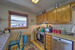 A kitchen with wooden cabinets, a stainless steel range, a dishwasher, and a window overlooking a residential area. - Walk to New River Access! Family Cabin w/ Deck (Piney Creek)