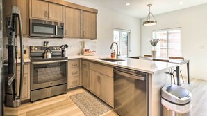 A modern kitchen with stainless steel appliances, wooden cabinets, and a large island. - Spacious St. George Townhome w/ Grill & Views! (St. George)