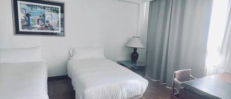 A hotel room with two single beds, a desk, a chair, a lamp, and a picture on the wall.