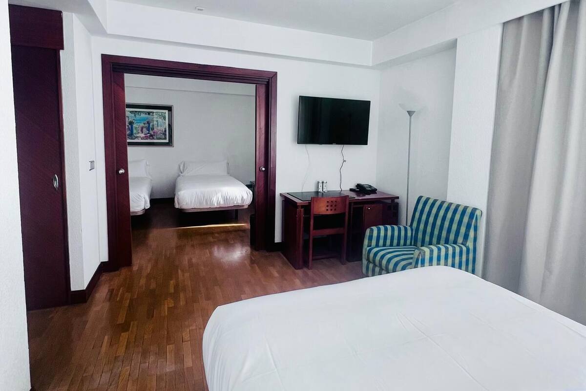 Une chambre d’hôtel avec un grand lit, un bureau, une chaise, une télévision et une porte donnant sur une autre pièce.