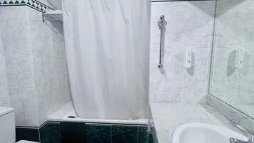 Un baño con inodoro blanco, ducha con cortina blanca, bañera y lavamanos con espejo encima.