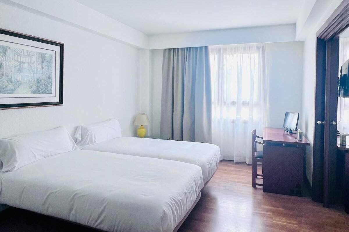 Une chambre d’hôtel avec deux lits, un bureau, une chaise et une fenêtre avec des rideaux.
