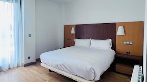 A modern hotel room with a large bed, wooden headboard, bedside lamps, and a large window with curtains. - Hotel ITC Ciudad de Haro (Haro)