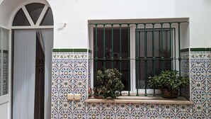 A window with green metal bars, a tiled wall with a geometric pattern, and potted plants on the windowsill. - Casa Marialuisa - Casa original en el Casco antiguo (Barbate)