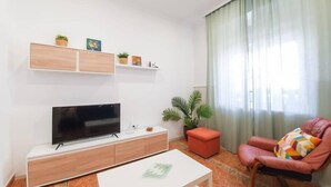 A living room with a flat-screen TV, a white coffee table, a red armchair, and a potted plant. - Casa Marialuisa - Casa original en el Casco antiguo (Barbate)