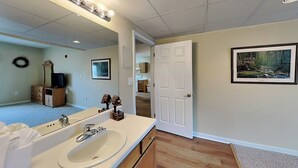 Une salle de bain avec un grand miroir, un lavabo, des meubles en bois et une porte donnant sur une autre pièce.
