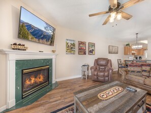 A living room with a fireplace, a leather armchair, a sofa, a coffee table, and a television mounted on the wall.