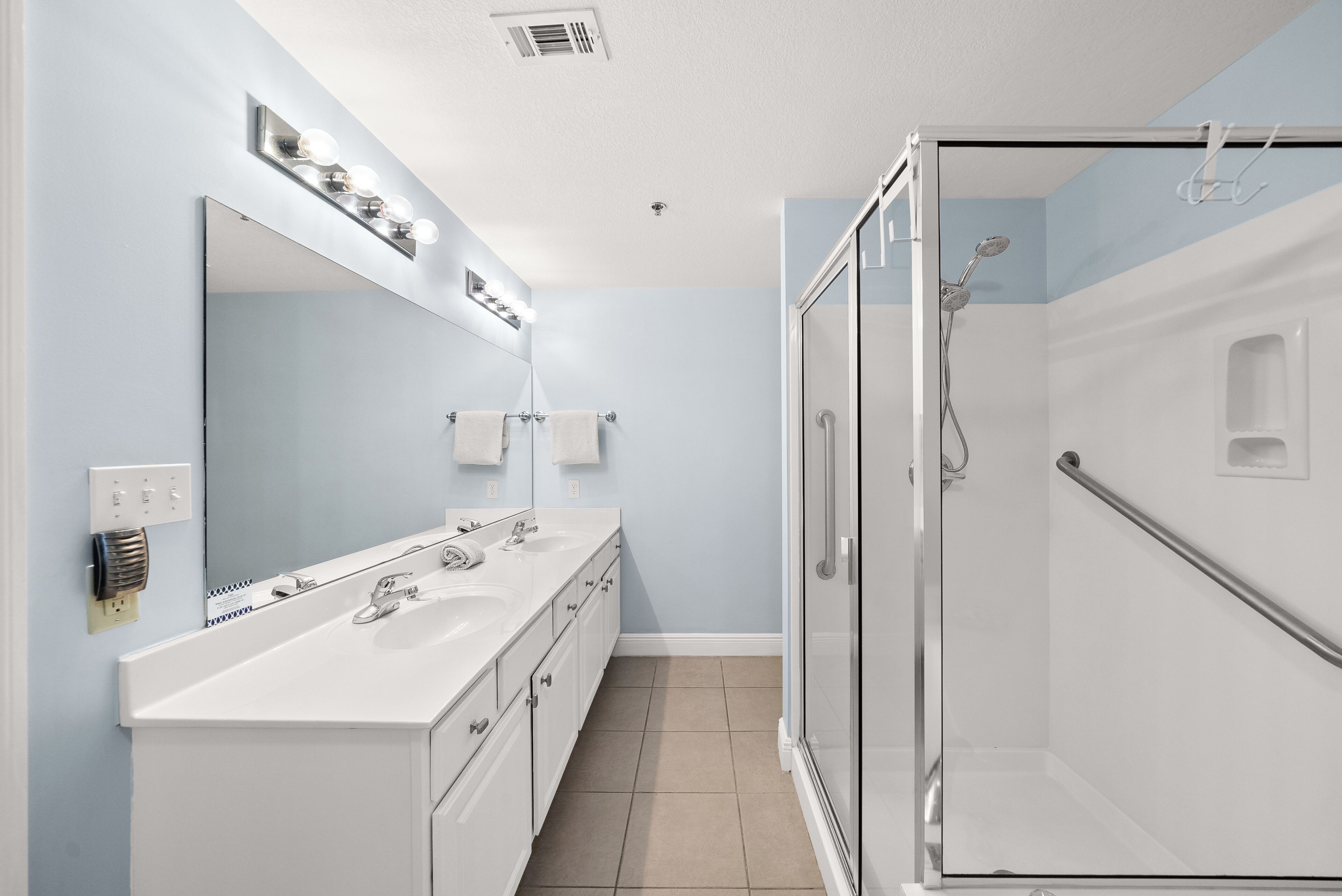 Un baño con tocador doble lavamanos, un espejo grande y cabina de ducha con paredes de cristal.