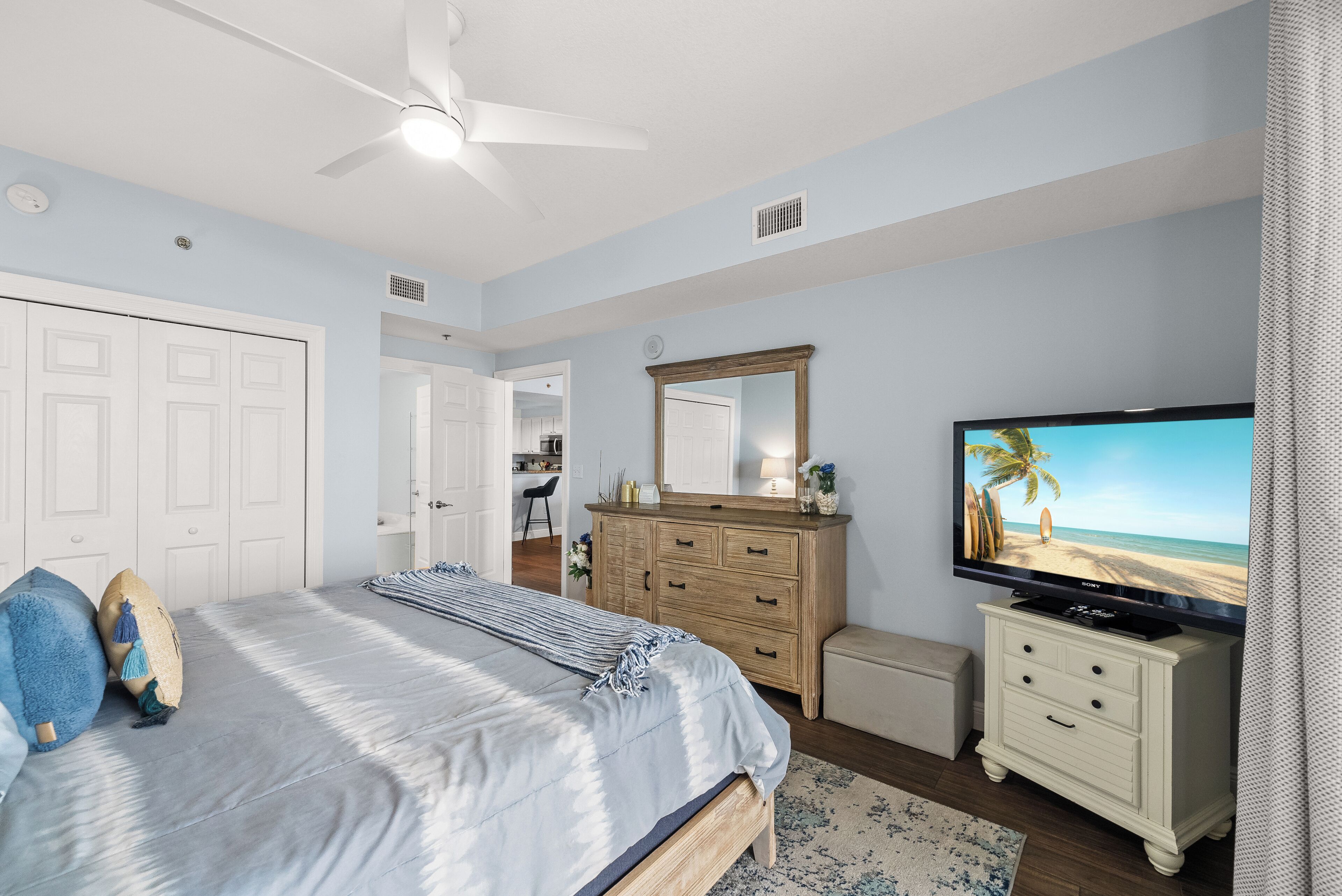 A bedroom with a bed, dresser, TV, and ceiling fan.