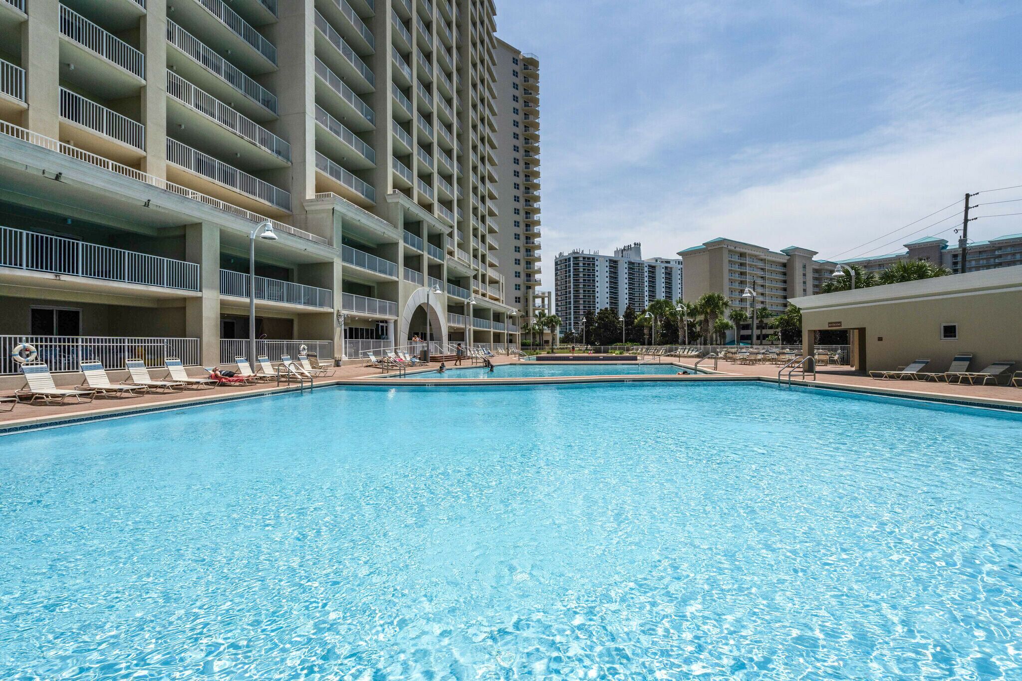 Una piscina con sillas de descanso y un edificio de varios pisos con balcones.