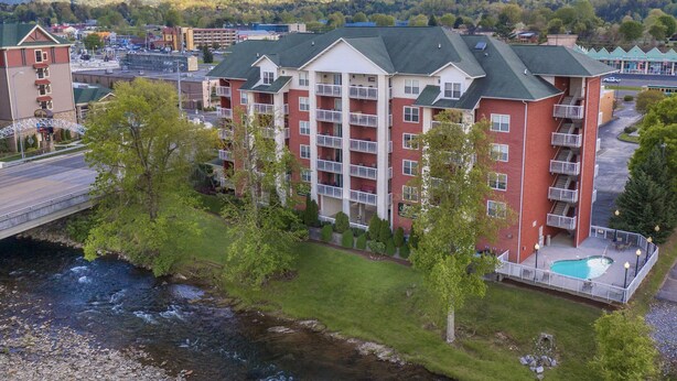 Ett hotell med flera våningar, en swimmingpool och ett läge nära en flod, omgivet av grönska och berg.