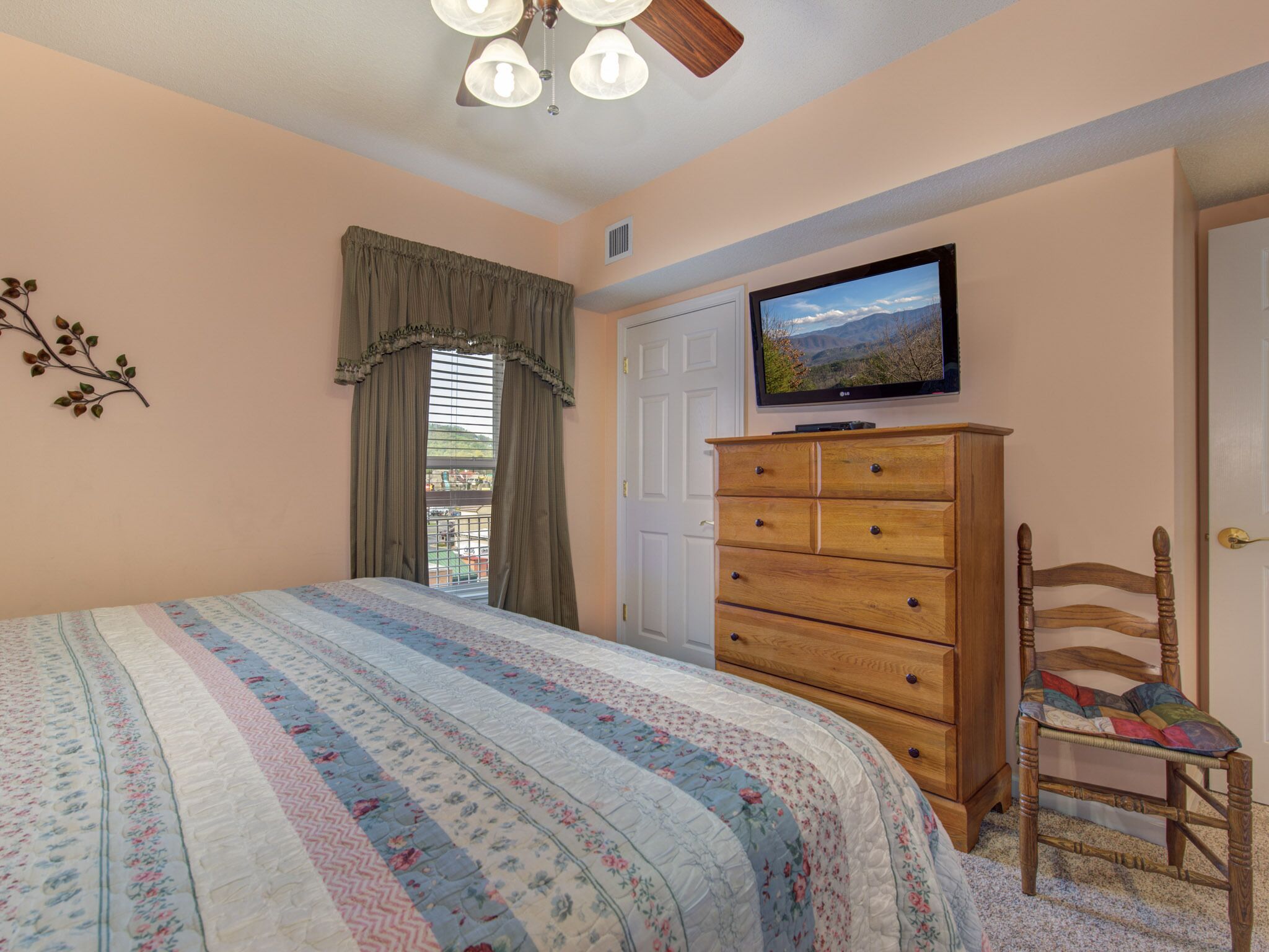 Un dormitorio con cama, cómoda, televisor y ventana con cortinas.