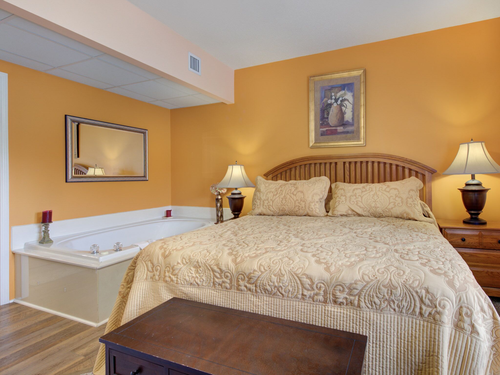 A bedroom with a large bed, a bathtub, and a wooden nightstand with lamps.