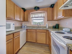 A compact kitchen with wooden cabinets, a microwave, a coffee maker, and a stove.