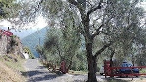 A rural road with a stone wall on one side and a red gate leading to a parked car.