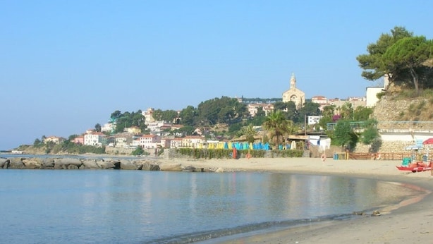 A coastal town with a prominent church on a hill, a sandy beach, and a calm sea.