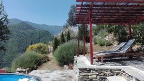A pool area with a pergola and lounge chairs overlooking a mountainous landscape.
