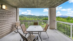 Un balcone con tavolo e sedie, vista su colline e montagne verdi, e un soffitto in cemento.