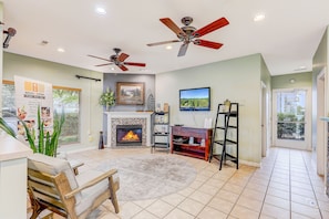 Sala de estar con chimenea, ventiladores de techo, televisor y vistas al exterior.