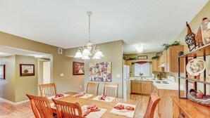 Un'area pranzo con un tavolo e sedie in legno, un lampadario e una cucina sullo sfondo.