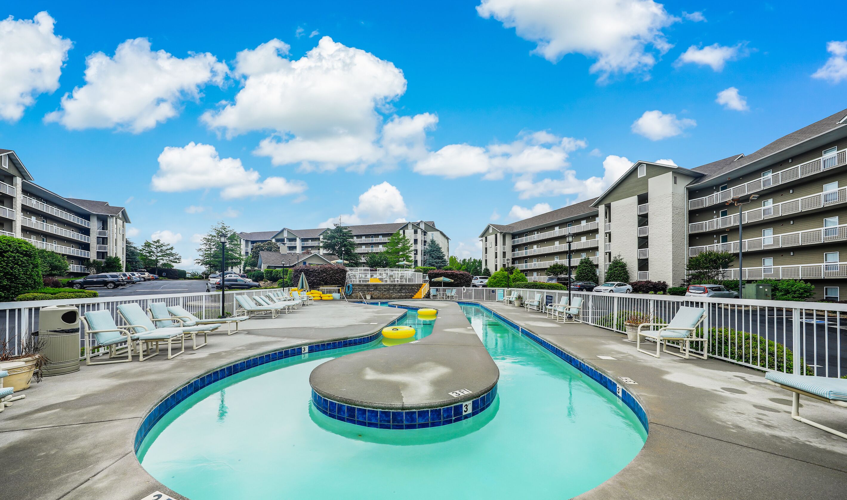 A swimming pool with lounge chairs and a small hot tub, surrounded by apartment buildings.