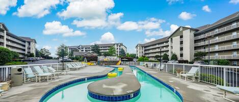 A swimming pool with lounge chairs and a small hot tub, surrounded by apartment buildings.