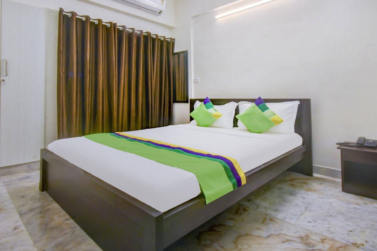 Una habitación de hotel con una cama, una mesita de noche, una cortina y un aire acondicionado instalado en la pared.